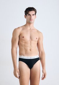 Schwarze Baumwollslips mit einem weißen Bund, der rot-blauen Logo-Text trägt. Das Design ist enganliegend und hat eine glatte Textur.