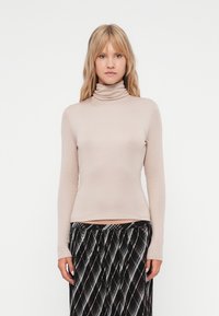 Beżowy sweter typu golf wykonanego z miękkiego materiału, z długimi rękawami i dopasowanym krojem. Połączony z wzorzystą spódnicą w czarno-białe desenie.