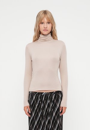 Beige turtleneck top lavet af blødt stof, med lange ærmer og en tætsiddende design. Sammen med en mønstret sort og hvid nederdel.