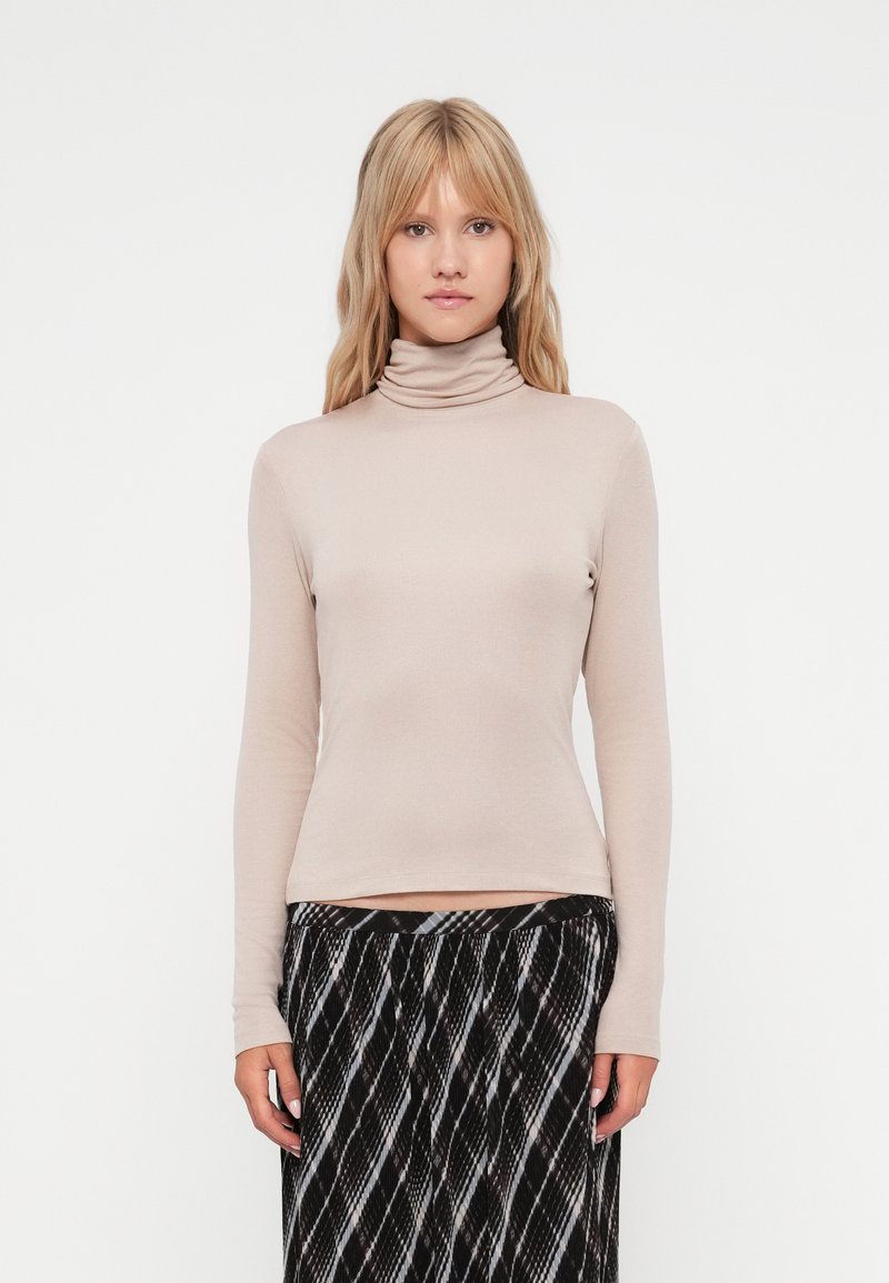 Beżowy sweter typu golf wykonanego z miękkiego materiału, z długimi rękawami i dopasowanym krojem. Połączony z wzorzystą spódnicą w czarno-białe desenie.