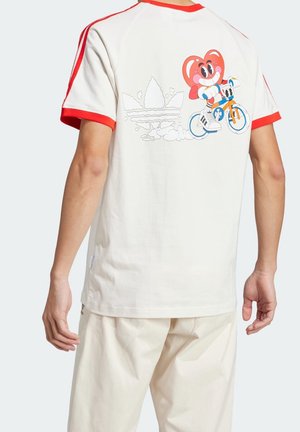 T-shirt en coton crème avec des accents rouges et des manches courtes. Représente un personnage de dessin animé à vélo et un logo graphique au dos.