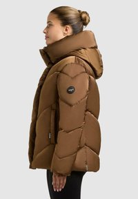 Giacca a vento marrone con un grande cappuccio, caratterizzata da un design a rombi cuciti, polsini a coste e una toppa con logo sulla manica.