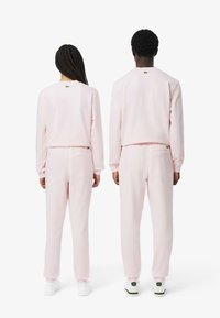 Roze sweatshirt en joggingset, gemaakt van zachte stof, met ribgebreide boorden, elastische tailleband en een klein logopuntje op de achterkant.