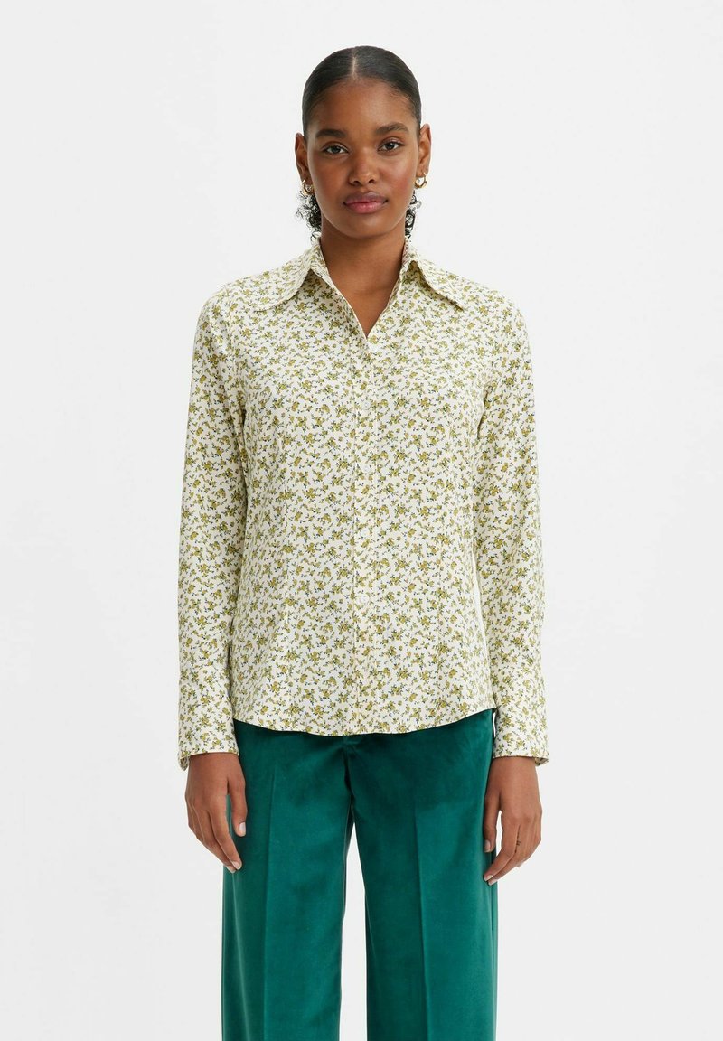 Langärmlige Bluse in hellem Creme mit einem kleinen grünen Blumenmuster. Verfügt über einen spitzen Kragen und einen geraden Saum. Weiches, glattes Material.
