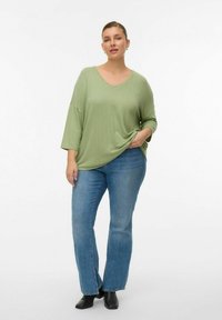 Haut en maille côtelée vert clair avec un col en V et une coupe décontractée, associé à un jean bleu à jambe droite et des bottines noires.