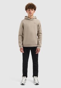 Beige sweatshirt met capuchon, geribbelde manchetten en klein logo op de borst, gecombineerd met zwarte broek en zilveren sneakers. Glad textuur van de stof.