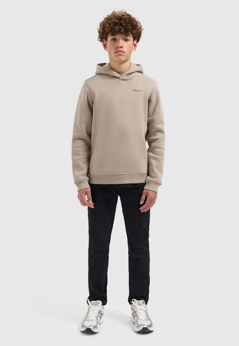 Beige sweatshirt met capuchon, geribbelde manchetten en klein logo op de borst, gecombineerd met zwarte broek en zilveren sneakers. Glad textuur van de stof.