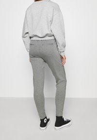 Sudadera gris y pantalones de chándal gris a juego con un corte slim. Los pantalones de chándal tienen acentos laterales texturizados y se emparejan con zapatillas altas negras.