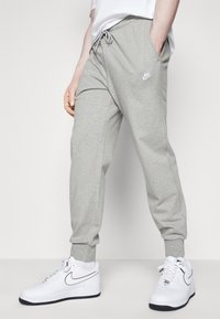 Gray sweatpants with an elastic waistband and drawstring. Features side pockets and a small white Nike logo on the thigh. Paired with white sneakers.