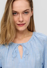 Helles blau und weiß gestreiftes Blusenshirt mit rundem Ausschnitt und Bindedetail. Weicher, leichter Stoff mit lockerem Schnitt.