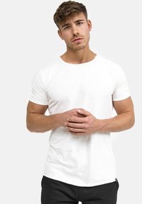 White short-sleeve t-shirt made of a textured fabric, featuring a round neckline and a slim fit, worn with black pants.