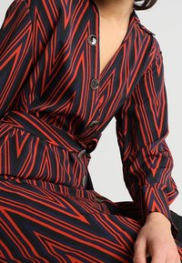 Abito con motivo zigzag rosso e blu navy realizzato in tessuto leggero, con chiusura a bottoni e vita con cintura per una maggiore definizione.