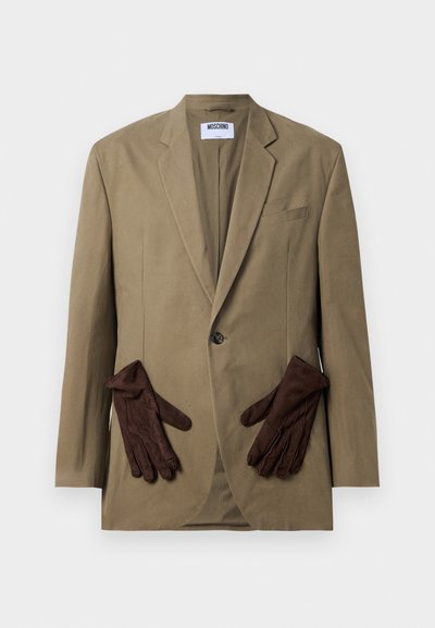 Khaki-Blazer mit einem einzigen Knopf, mit Revers und zwei Vordertaschen. Braune Handschuhe im Taschenfach platziert. Glattes Material, strukturierter Schnitt.