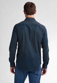 Camicia a maniche lunghe blu navy con colletto a punta e design aderente. Il tessuto testurizzato presenta piccoli motivi circolari bianchi.