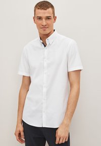 Camisa blanca de manga corta, hecha de algodón, con cuello botón, placket frontal con botones y dobladillo curvado. Diseño simple y limpio.