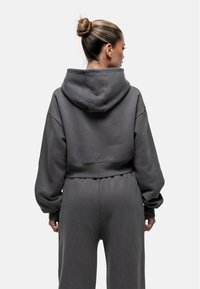 Korte hoodie in donkergrijs, met oversized mouwen en een zachte textuur. De capuchon is vastgenaaid; geribbelde tailleband.