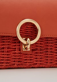 Rode geweven handtas met een glad leren bovenkant, gouden ronde hardware en een gestructureerd ontwerp aan de onderkant. Compact met unieke accenten.