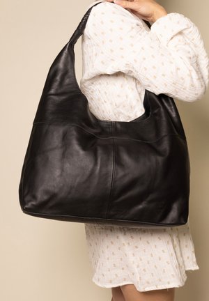 Black leather hobo bag with a smooth texture, curved design, and wide shoulder strap. Features a seam line across the middle.