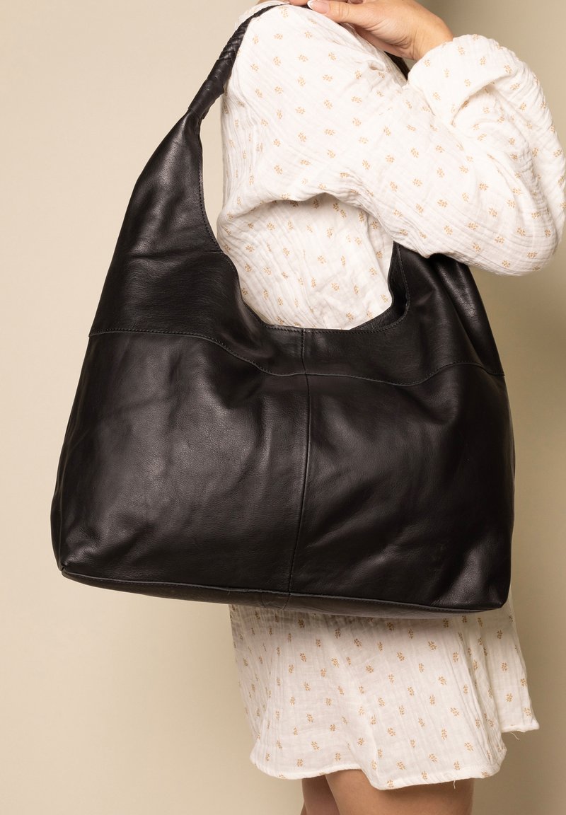 Black leather hobo bag with a smooth texture, curved design, and wide shoulder strap. Features a seam line across the middle.