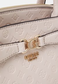 Lys rosa faux læder håndtaske med præget logo mønster, guldfarvet hardware, lynlåslukning og front branding detalje "GUESS EST 1981."