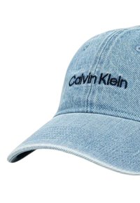 Cappellino da baseball in denim di colore azzurro chiaro, con visiera curva e ricamo del logo "Calvin Klein" in nero sulla parte anteriore. La texture è leggermente ruvida.