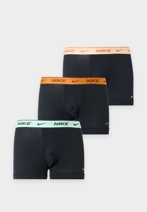 Atletisk mand stående barfodet iført sorte Nike boxer briefs med beige taljebånd mod en ensfarvet hvid baggrund.