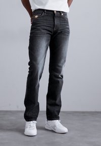 Blugi din denim negri cu o spălare estompată, croială dreaptă, buzunare frontale și detalii de cusătură aurie. Purtați cu pantofi sport albi.