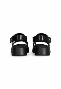Sandales noires avec des brides en cuir verni brillant et une semelle plateforme noire mate, épaisse. Équipées d'une bride à la cheville réglable pour un ajustement sécurisé.