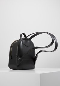 Mochila negra de cuero con una forma estructurada, cremallera dorada, correas ajustables y un acabado texturizado. Presenta un diseño minimalista y un bolsillo lateral.