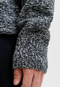 Ukra�šeni rebrasti manžetni džemper u crno-bijelim tonovima; ima rebrasti rub i blago labav kroj, ističući složene uzorke.