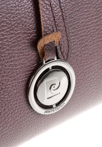 Primo piano di un logo circolare argentato Pierre Cardin attaccato a pelle marrone texturizzata con cinturini cuciti.