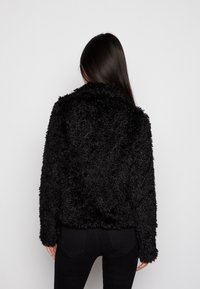 Svart, fluffig fuskpälsjacka med krage, lös passform och långa ärmar. Enfärgad design utan synliga knäppningar eller dekorationer.