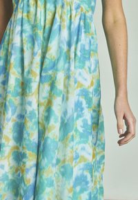 Maxi sukienka w niebiesko-zielony wzór tie-dye, z delikatnymi fałdami, wykonana z lekkiego materiału, o luźnym kroju.