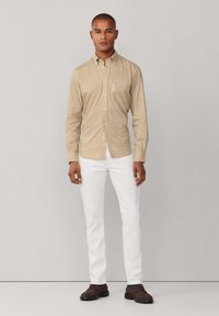 Camisa de botones en patrón de cuadros marrón y beige; mangas largas; pantalones blancos; zapatos marrones; ajuste casual.