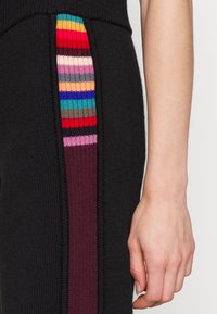 Zwarte gebreide broek met verticale strepen in rood, roze, paars, blauw en groen. Heeft een geribbelde textuur en een contrasterend zijpaneel.
