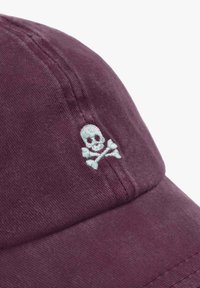 Gorra de algodón color burdeos con un diseño bordado de calavera y huesos cruzados en azul claro. Textura suave con detalles de costura visibles.