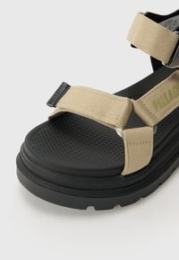 Smeđi tkaninski remeni sandale s teksturiranom crnom gumenom petom, s podesivim trakama i metalnim detaljima za sigurnu prilagodbu.