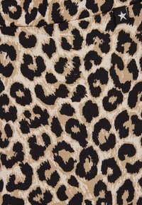 Leopardmönstrad tyg med en beige bakgrund och svarta fläckar. Materialet verkar texturerat med ett stickat mönster. Stjärnformad etikett synlig.