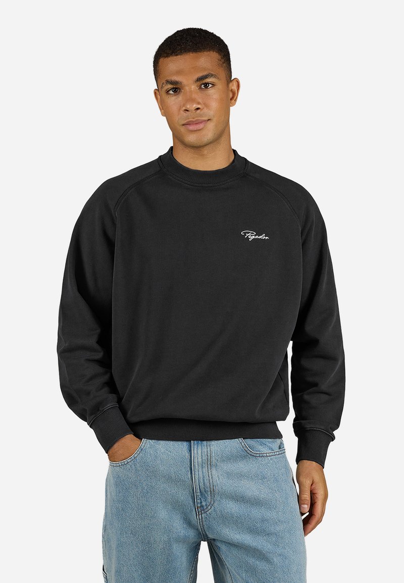 Sort sweatshirt med raglanærmer, ribbet krave og manchetter. Har et lille hvidt logo på brystet, parret med lyseblå jeans.