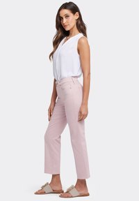 Pantalones de tiro alto en rosa claro con un diseño de pierna recta, combinados con una blusa sin mangas blanca y sandalias de dedo beiges.