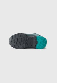 Terrengsko såle med et robust svart gummidesign og dype spor, aksentuert av en teal seksjon ved hælen for forbedret grep.