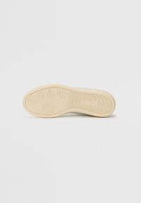 Semelle de sneaker en caoutchouc crème avec des motifs circulaires et texturés, présentant un bord lisse et des sections avec relief pour une meilleure adhérence.