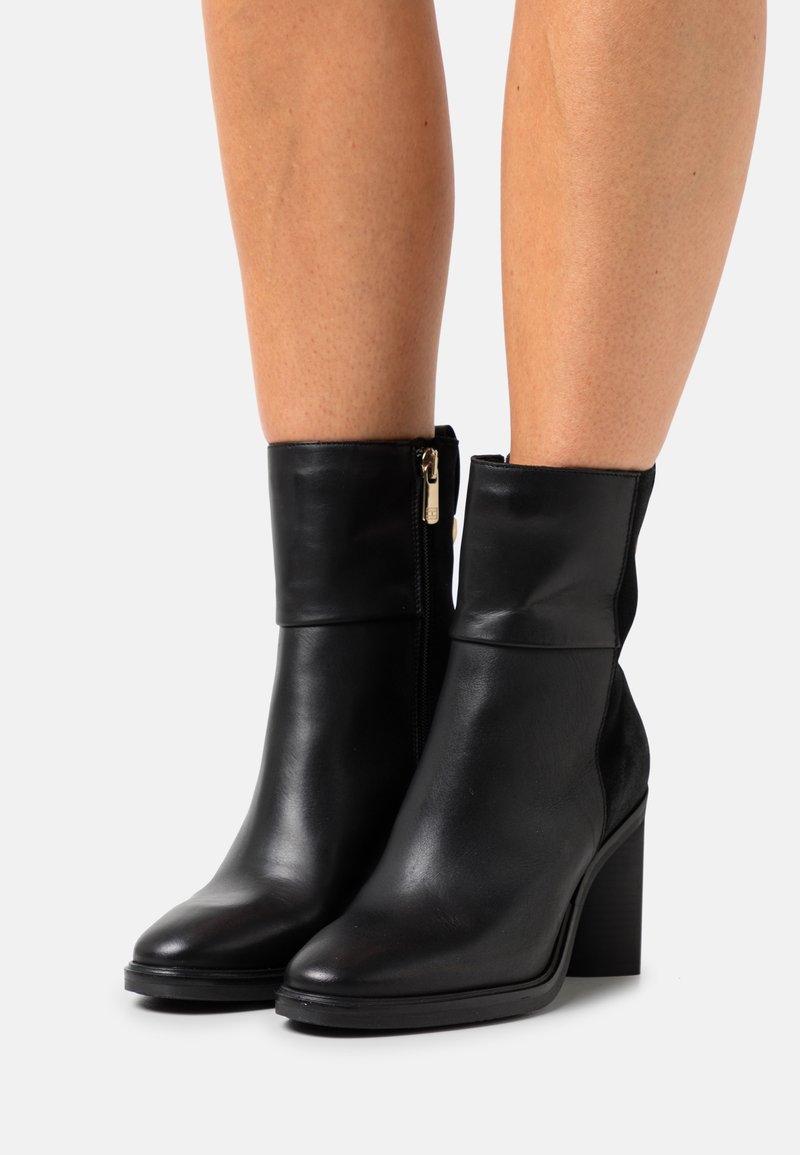 Bottes à cheville en cuir noir avec un large revers, une fermeture éclair latérale et un talon bloc. Texture lisse et design à bout arrondi.