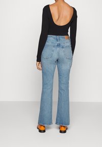 Top negro de manga larga con escote en la espalda profundo, combinado con jeans acampanados azul con cintura alta y dos bolsillos traseros. Sandalias de plataforma marrones.