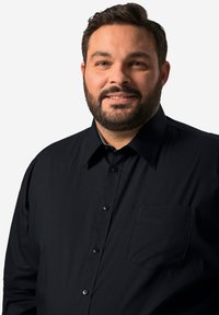 Zwarte overhemd met knopen, voorzien van een zak, gestructureerde kraag en een zachte textuur. Het overhemd wordt gedragen door een persoon met een baard.