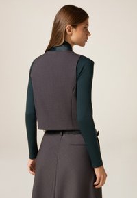Graues, kurzes Top mit glatter Textur, kombiniert mit einem dunkelgrünen Langarmhemd. Verfügt über ein dezentes Muster und eine schlichte Silhouette.