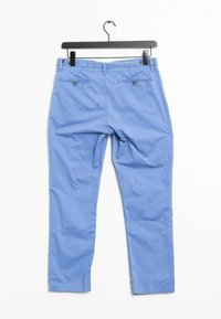 Světle modré bavlněné kalhoty visící na černém ramínku, s dvěma knoflíkovými kapsami na zadní straně a přímým střihem nohavic.