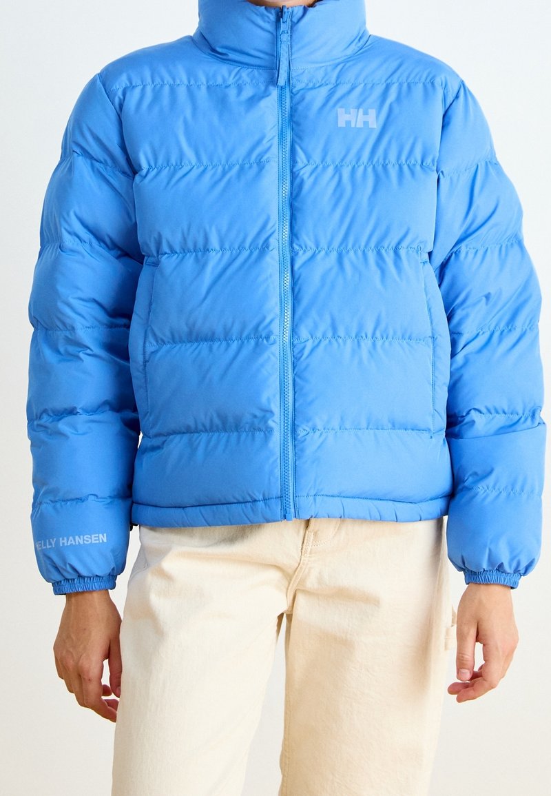 Ljusblått puffer-jacka med hög krage, dragkedjestängning och elastiska ärmslut. Har logodetaljer på bröstet och ärmen.