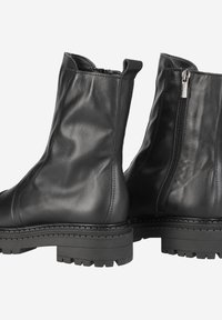 Bottines noires en cuir avec une finition mate, semelles en caoutchouc épaisses et fermetures éclair latérales. Présente un design épuré avec un minimum de coutures.