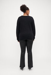 Črn oversized pulover z mehko teksturo, z okroglim izrezom in podrobnimi akcenti na rokavih. V kombinaciji s črnimi širokimi hlačami.